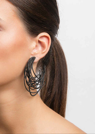 Close-up of a person wearing a large, intricate black hoop earring against a plain background