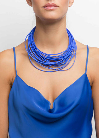 Woman wearing a blue necklace and dress against a plain background
