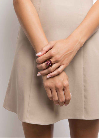 Woman wearing a beige dress and purple Theia ring, holding her hands together with a plain background.