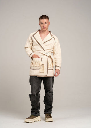 Person wearing a cream-colored robe with a belt and dark pants on a plain background