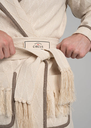 Beige robe with brown accents and fringes, held by a person, on a plain background.