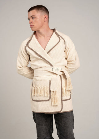 Man wearing a cream-colored robe with a belt on a gray background