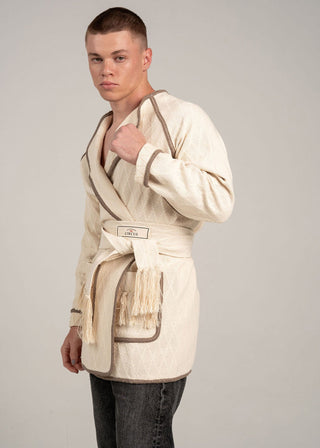 Man wearing a beige bathrobe with a belt on a plain background