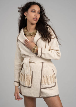 Woman wearing a beige robe with fringe details on a gray background