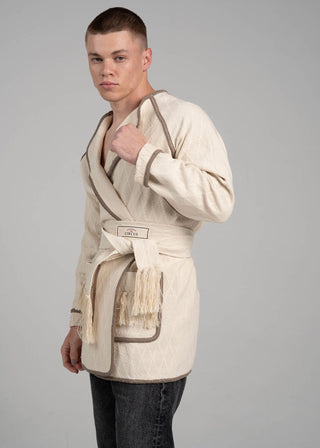 Person wearing a beige robe with a belt on a gray background