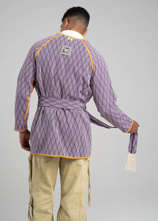 Person wearing a traditional outfit with a purple quilted jacket and beige pants on a gray background