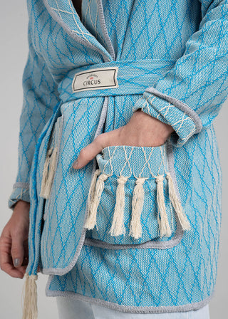 Blue textured bag with tassels and a visible brand label on a gray background