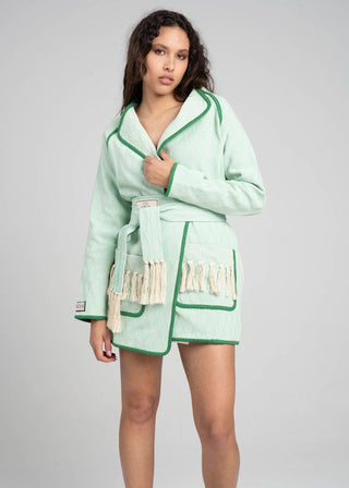 Woman wearing a light green robe with fringe details on a gray background