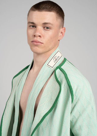 Man wearing a green cotton jacket with a brand label on a gray background
