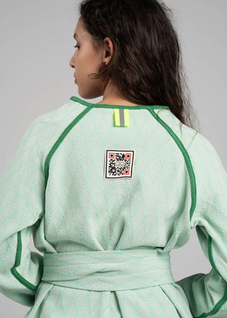 Person wearing a light green outfit with a QR code patch on the back against a gray background
