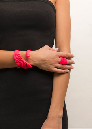 Person wearing a black strapless top with pink bracelets on a plain background