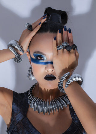 Person with dramatic makeup and jewelry, including a large metallic necklace and bracelets.