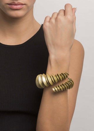 Person wearing a gold spiral bracelet on a plain background