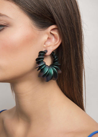 Close-up of a woman wearing green leaf-shaped earrings against a neutral background