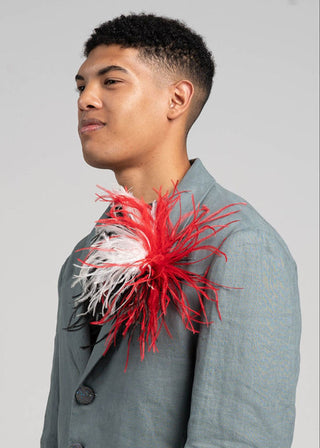 Man wearing a gray blazer with a red and white feathered accessory on a gray background