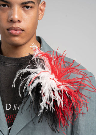 Person wearing a gray blazer with a red and white feathered accessory.