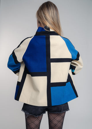 Person wearing a geometric-patterned jacket with blue, black, and beige colors on a plain background