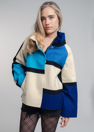 Woman wearing a color-blocked jacket with blue, beige, and black sections on a gray background