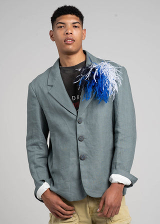 Person wearing a gray blazer with a decorative item on a plain background