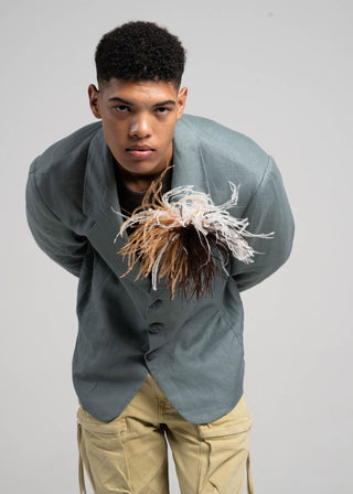 Person wearing a gray jacket with a unique design holding a plant-like object against a plain background
