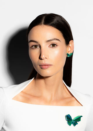 Woman wearing a white top with a green butterfly accessory against a white background