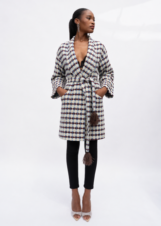 A woman models a long-sleeve patterned wrap coat with a tie belt and tassel, paired with black pants and clear high-heeled sandals, against a white studio background.