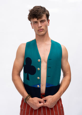 A male model wearing a sleeveless teal vest with a black club symbol and gold buttons, paired with red and white striped trousers, against a plain white background.