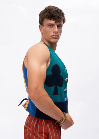 A man wearing a sleeveless knit vest with a teal and navy color-blocked design, featuring a large navy playing card club symbol on the front and gold buttons, paired with red and white striped shorts, against a plain white background.