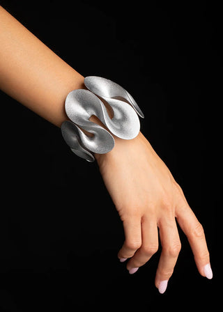A silver sculptural cuff bracelet worn on a person's wrist, shown against a solid black background.