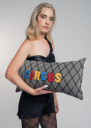 Woman holding a pillow with 'CIRCUS' in colorful letters against a plain background