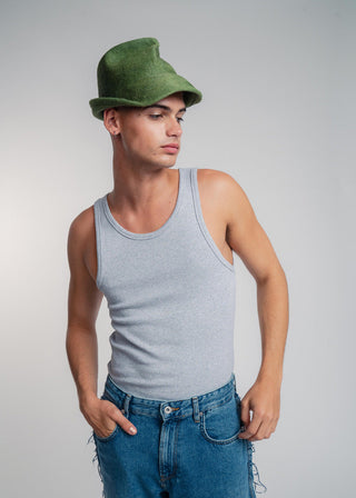 Person wearing a green hat, gray tank top, and blue jeans on a plain background