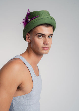 Man wearing a green hat with a feather against a plain background