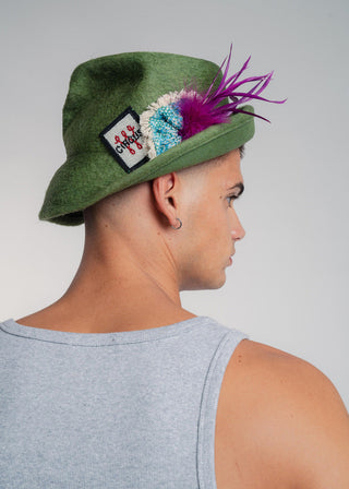 Person wearing a green hat with colorful feathers and a patch, on a plain background