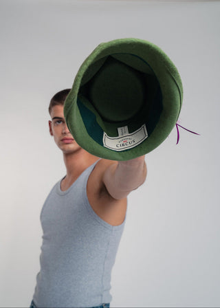Man holding a green felt hat with a brand label against a white background