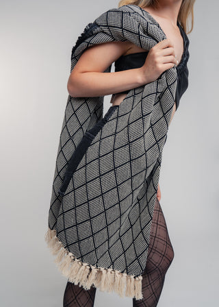 Woman wearing a black and white patterned scarf with tassels in a studio setting