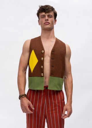 A male model wearing a brown vest with a yellow diamond and green band detail, paired with red and white striped trousers, against a plain white studio background.