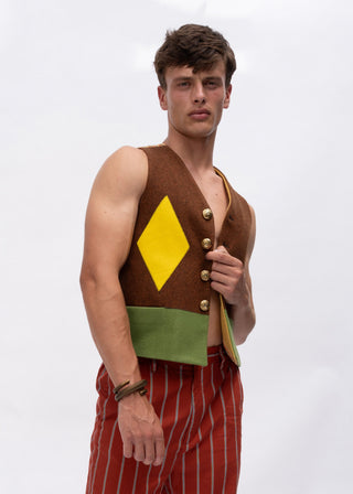A young man modeling a brown sleeveless vest with a yellow diamond and green band, paired with red and white pinstriped trousers, against a plain white studio background.