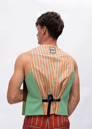 A man shown from the back wearing a sleeveless vest with a striped orange, yellow, and white back panel, sage green side panels, and a navy tie at the waist.