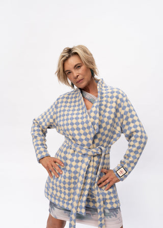 A woman modeling a long-sleeve patterned robe with a tie waist, featuring a cream and light blue diamond check design, set against a plain white studio background.