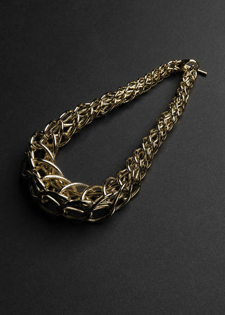 A chunky gold-toned chain necklace with a braided, interlocking link design, photographed on a dark charcoal background.