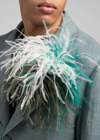 Person wearing a gray coat with a decorative feathered scarf in white and green.
