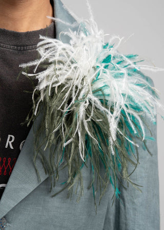 Close-up of a decorative brooch with white and green feathers on a gray background