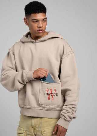 Person wearing a beige hoodie with a pocket design on a gray background