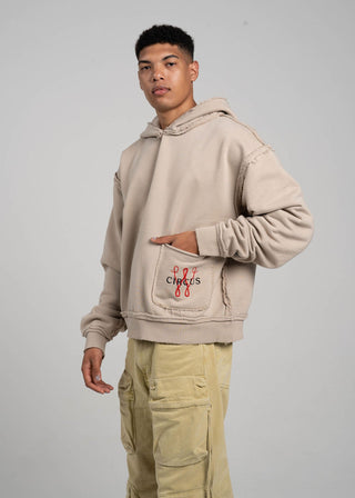 Person wearing a beige hoodie with a brand logo on a gray background