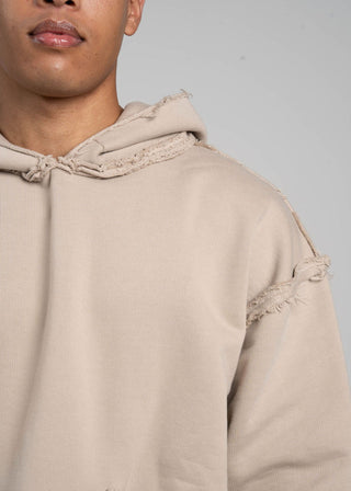Beige hoodie with distressed details worn by a person on a gray background