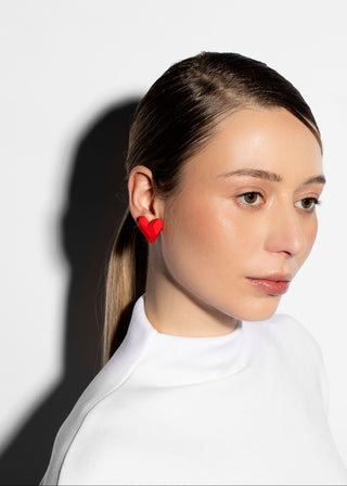 Woman wearing red heart-shaped earrings against a white background