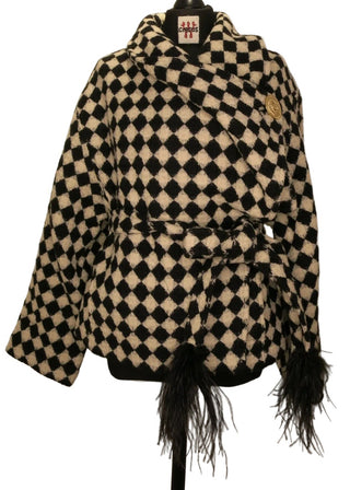 A black and white checkered coat with black feathers on the cuffs, displayed on a black mannequin torso against a plain beige background.