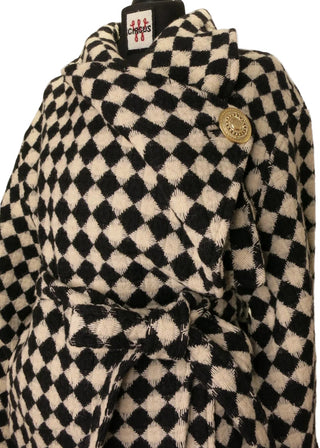 A close-up of a black and off-white checkered patterned garment, likely a jacket or coat, draped on a black hanger. A small gold button and a fabric brand tag are visible.