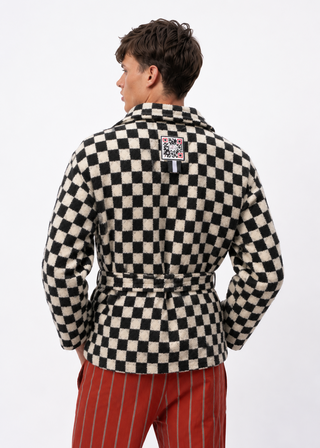 A man shown from the back wearing a black and cream checkered belted jacket and red pinstriped trousers, photographed against a plain white studio background.