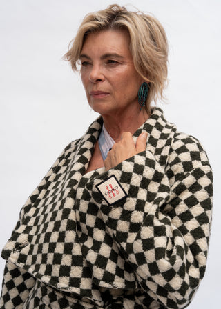A woman wearing a black and cream checkered fuzzy cardigan with a small embroidered patch on the sleeve, photographed against a plain light gray background.